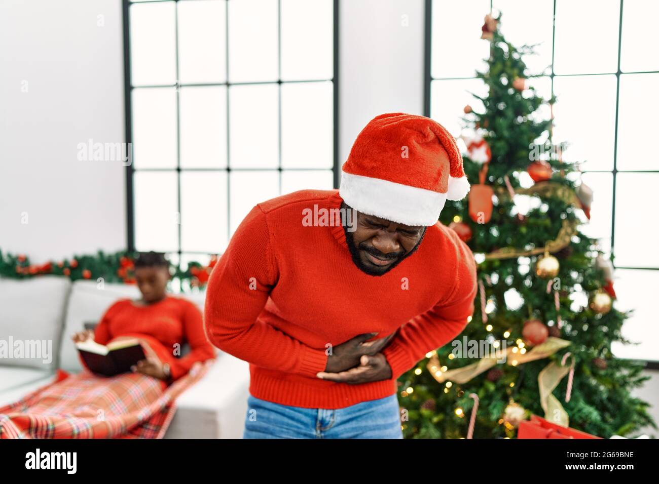 Junger afroamerikanischer Mann, der am weihnachtsbaum mit der Hand auf dem Bauch steht, weil Übelkeit, schmerzhafte Krankheit, Unwohlsein. Schmerzkonzept. Stockfoto