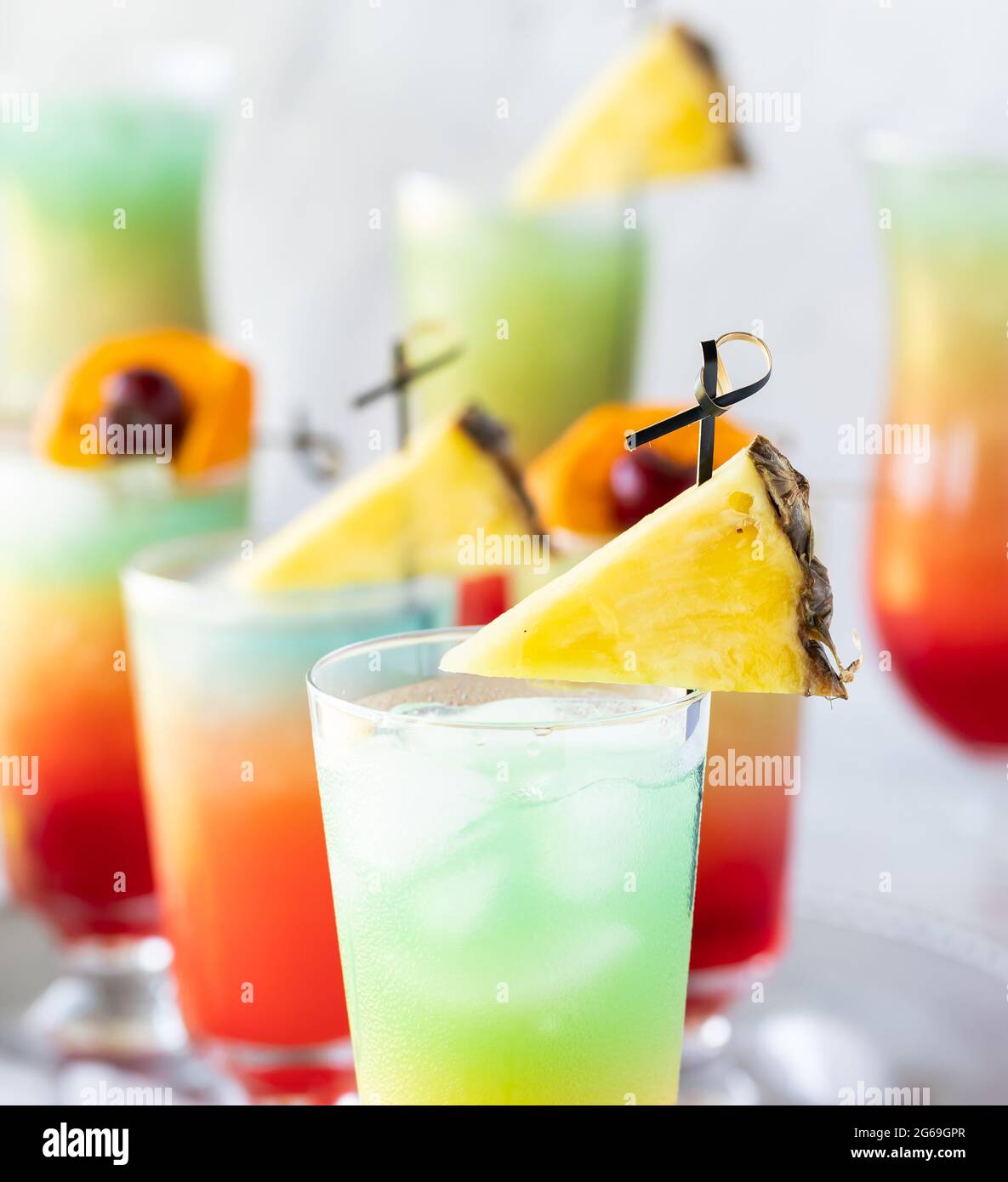 Nahaufnahme mehrerer farbenfroher eisiger Cocktails, garniert mit Ananaskeilen. Stockfoto