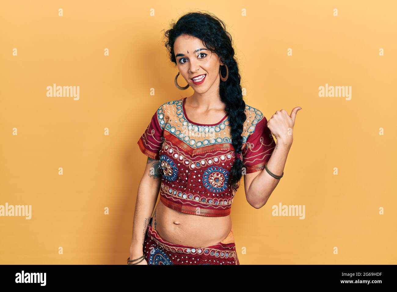 Junge Frau in Bindi- und bollywood-Kleidung, lächelnd, mit glücklichem Gesicht und mit dem Daumen nach oben zur Seite zeigend. Stockfoto