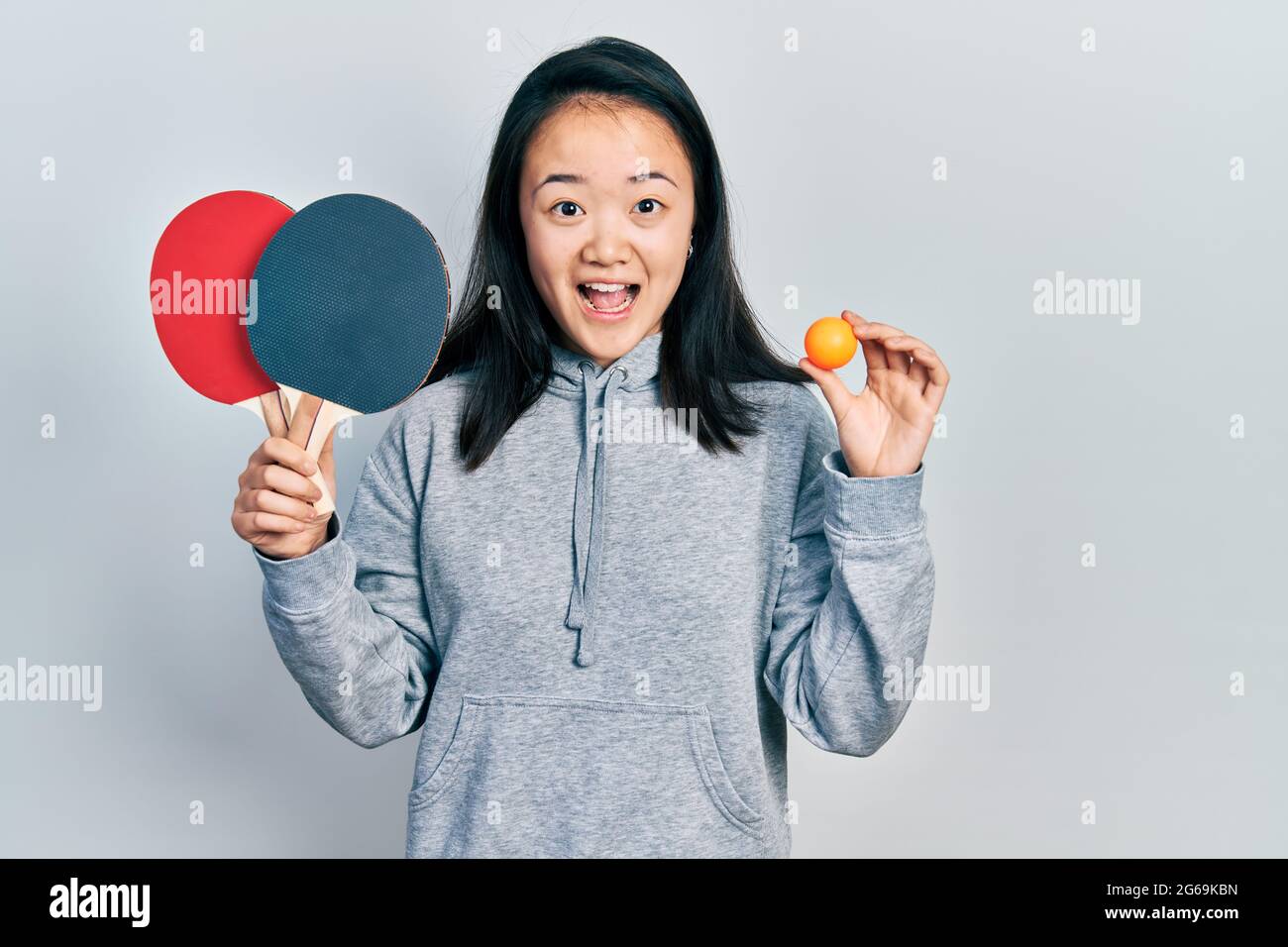 Junge chinesische Mädchen mit roten Ping-Pong-Schlägern und Ball feiern verrückt und erstaunt für den Erfolg mit offenen Augen schreiend aufgeregt. Stockfoto
