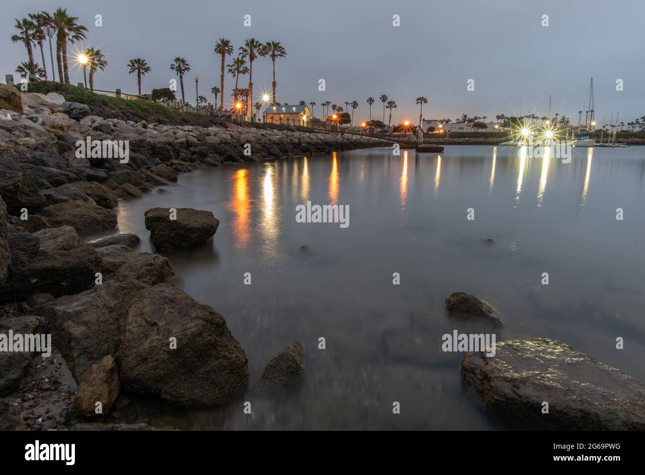 Glatte Oberfläche auf der Meeresbucht Wasser mit der Reflexion von Lichtern und Felsen am Morgen. Stockfoto