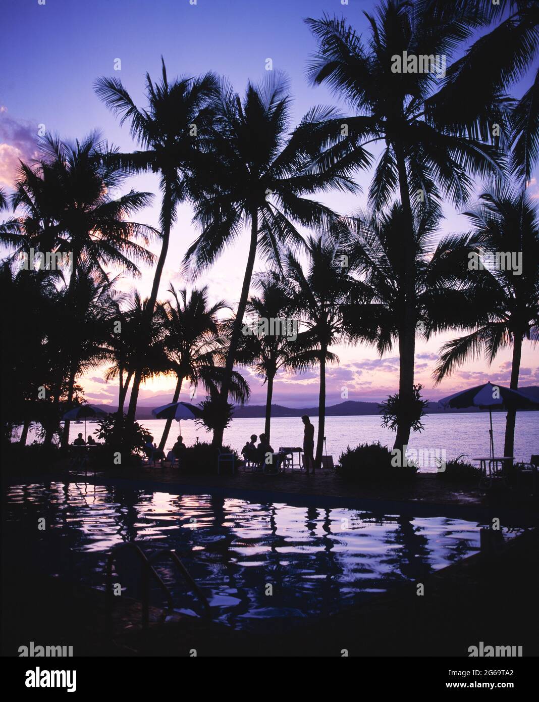 Australien. Queensland. Dunk Island. Menschen am Hotelpool mit Palmen bei Sonnenuntergang. Stockfoto