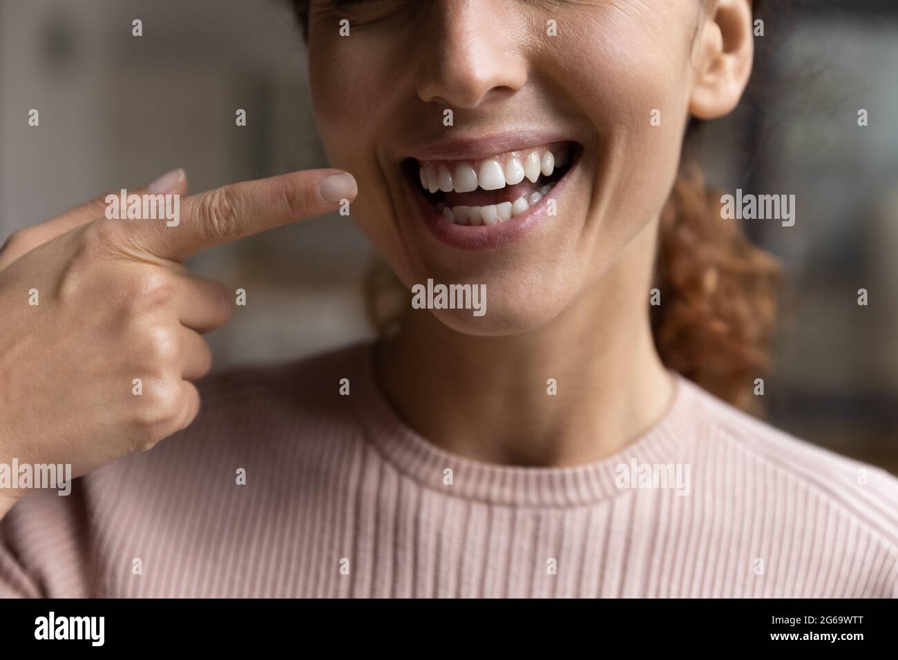 Glückliche junge Frau, die mit dem Finger auf ein weißes, toothy Lächeln zeigt. Stockfoto
