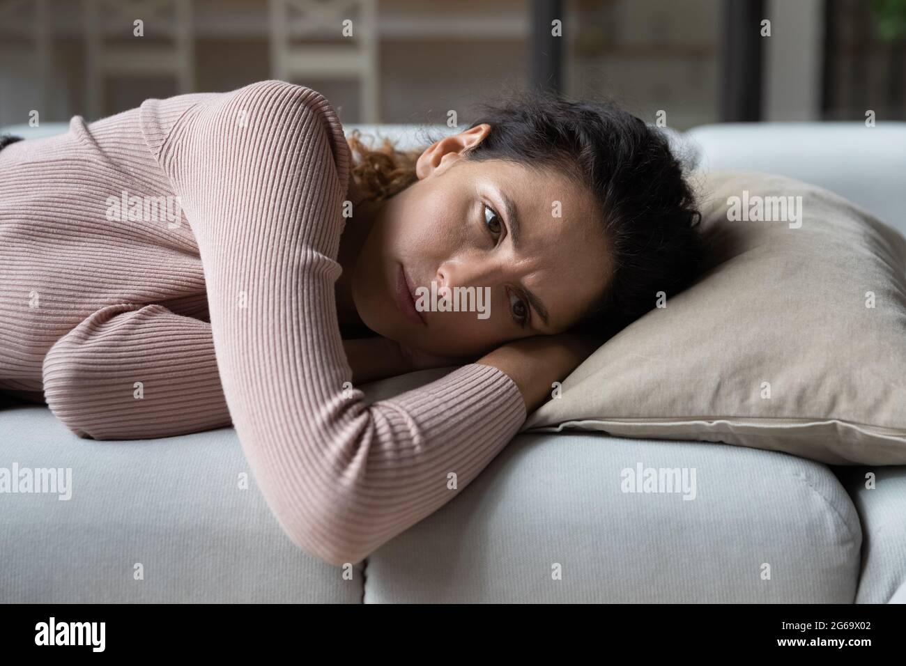 Unglückliche junge Frau, die sich gelangweilt fühlt und allein auf dem Sofa liegt. Stockfoto