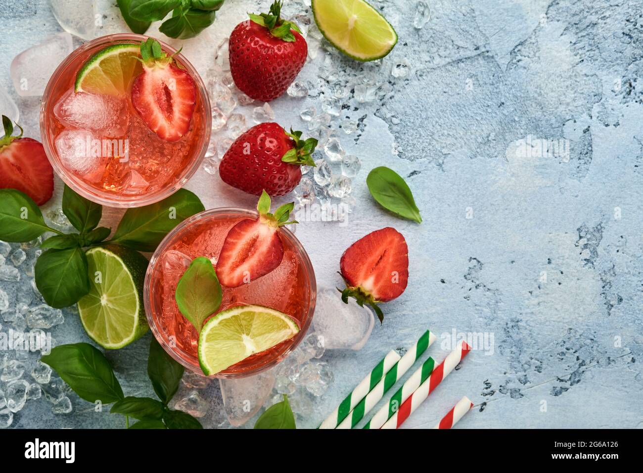 Zwei Gläser Punsch und frische Zutaten für die Herstellung von Limonade, infusem Detox-Wasser oder Cocktail. Erdbeeren, Limette, Minze, Basilikum, Eiswürfel und Shaker Stockfoto