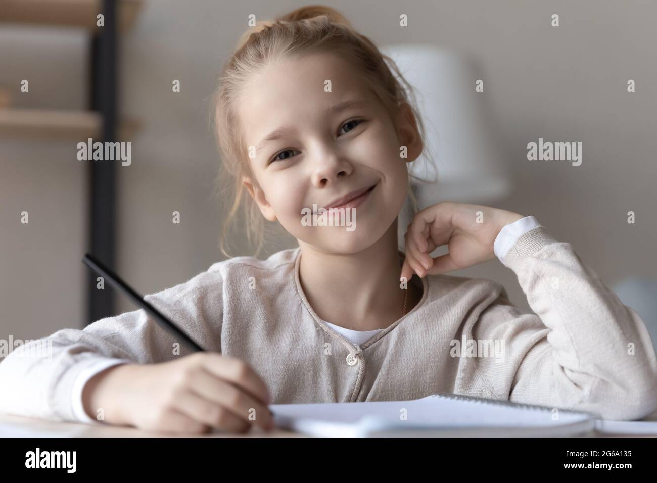 Kopfschuss Porträt lächelndes Mädchen Grundschulalter Schüler am Schreibtisch Stockfoto