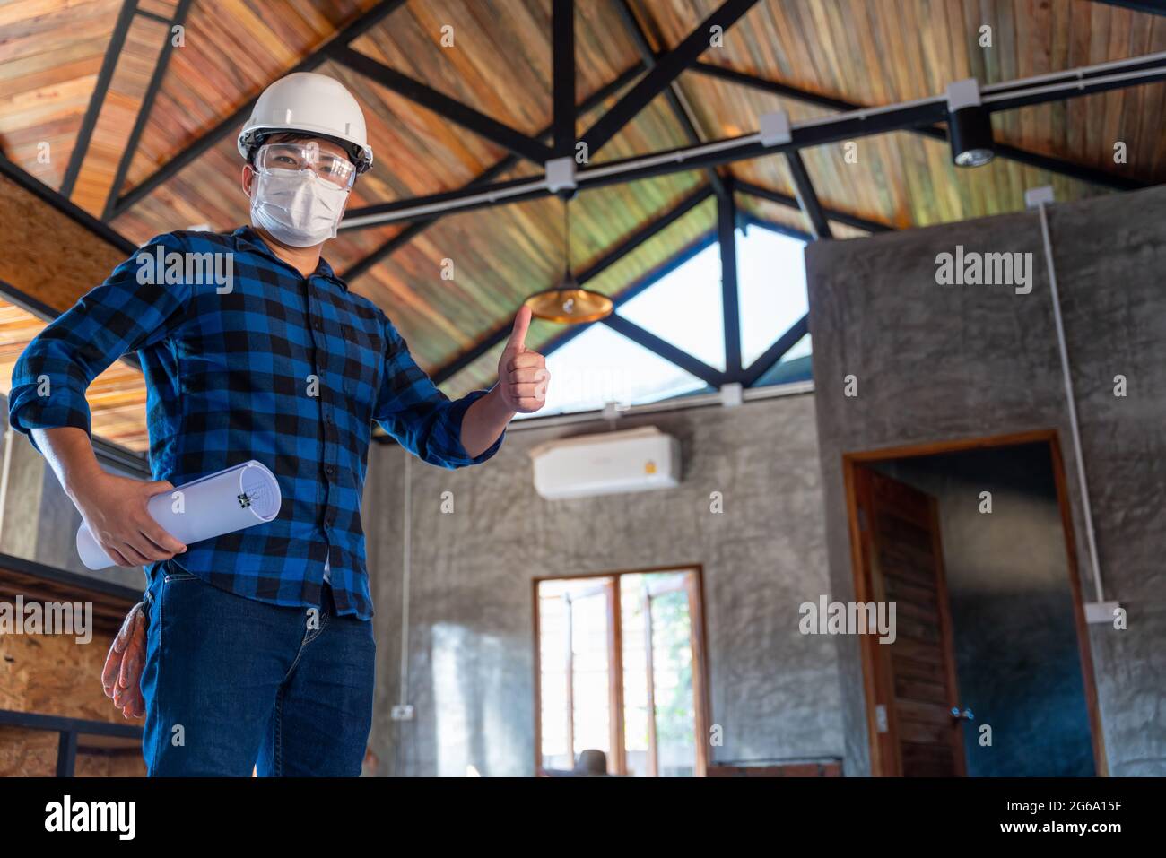 Ein glücklicher asiatischer Konstruktionsingenieur inspiziert die Holzstruktur unter dem Dach auf der Baustelle oder auf der Baustelle eines Hauses. Stockfoto