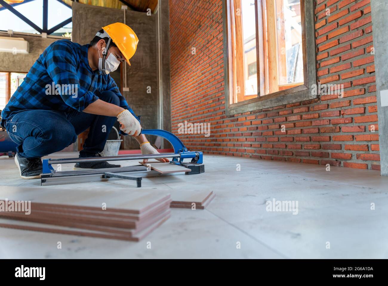 Asiatischer Ziegel-Handwerker auf der Baustelle, schneidet Arbeiter eine große Fliesenplatte während des Baus eines Hauses, Bodenfliesen Schneideausrüstung Stockfoto