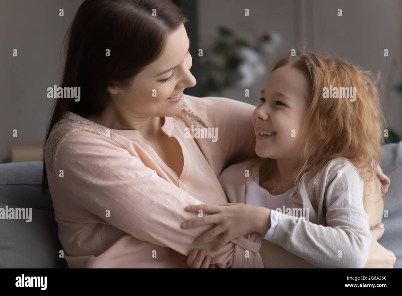 Fürsorgliche Pflegemutter umarmen adoptierte Mädchen im Wohnzimmer Stockfoto