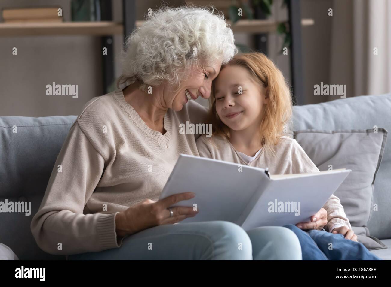 Die alte Großmutter und die Enkelin aus dem Jugendalter lasen auf dem Sofa ein Buch Stockfoto