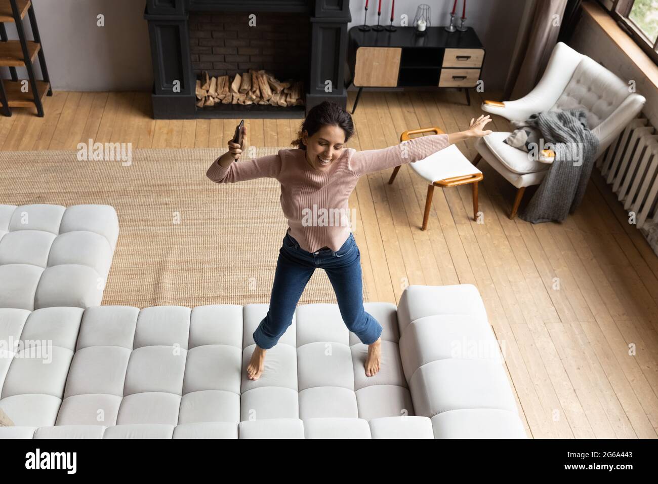 Emotional energische junge hispanische Frau, die auf dem Sofa tanzt. Stockfoto