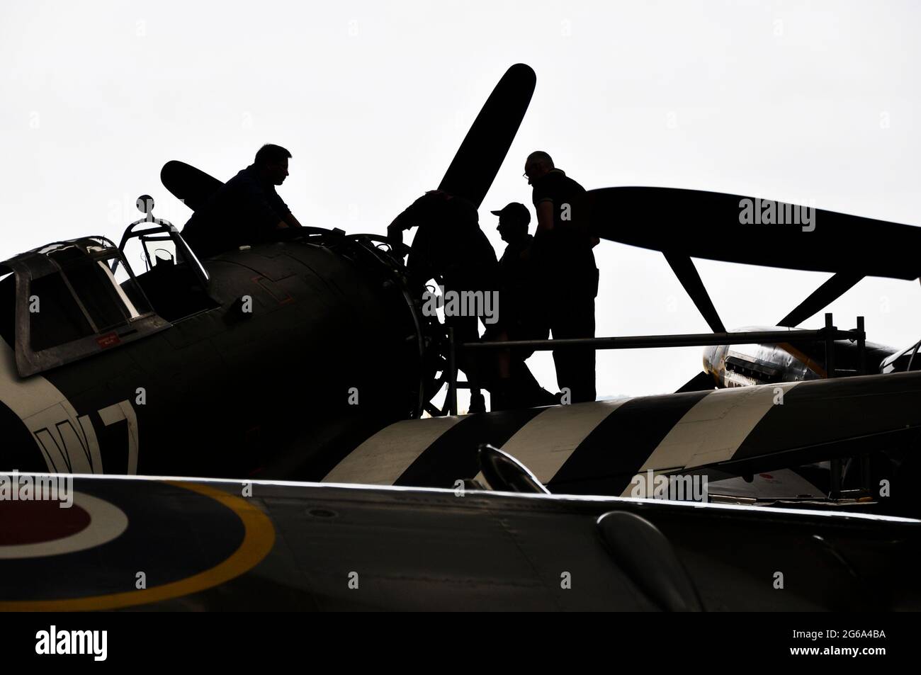 Silhouette von Ingenieuren, die an Kampfflugzeugen des Zweiten Weltkriegs im Hangar in Duxford arbeiten. Silhouetten von Mechanikern, die am Motor eines P-47 arbeiten Stockfoto