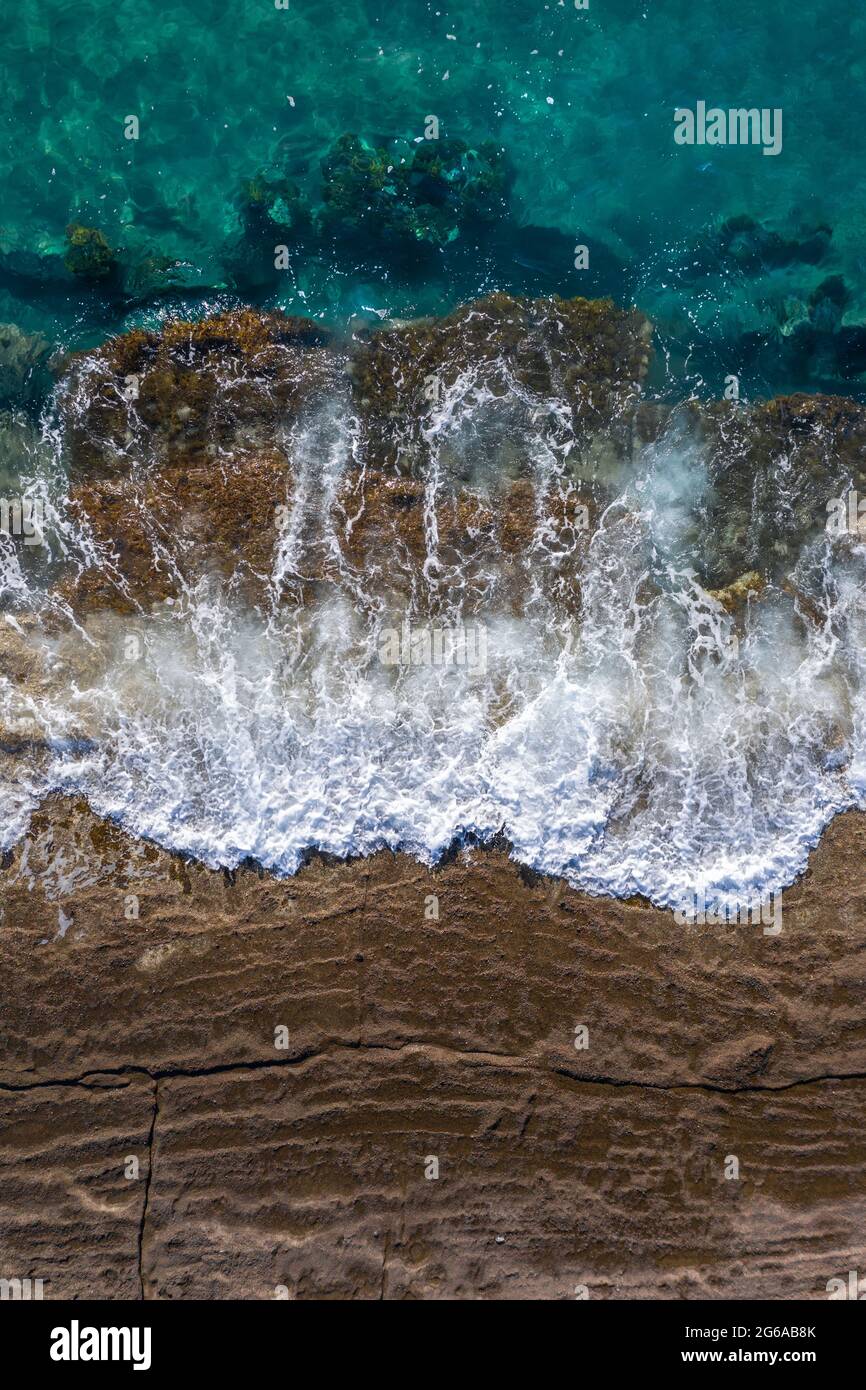 Wellen brechen auf braunen Klippenfelsen mit steigender Flut, Drohnenperspektive direkt darüber Stockfoto