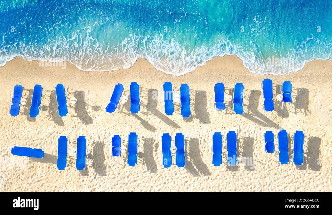 Zwei Reihen leerer blauer Sonnenliegen am gelben Sandstrand, Luftpanorama von direkt oben Stockfoto