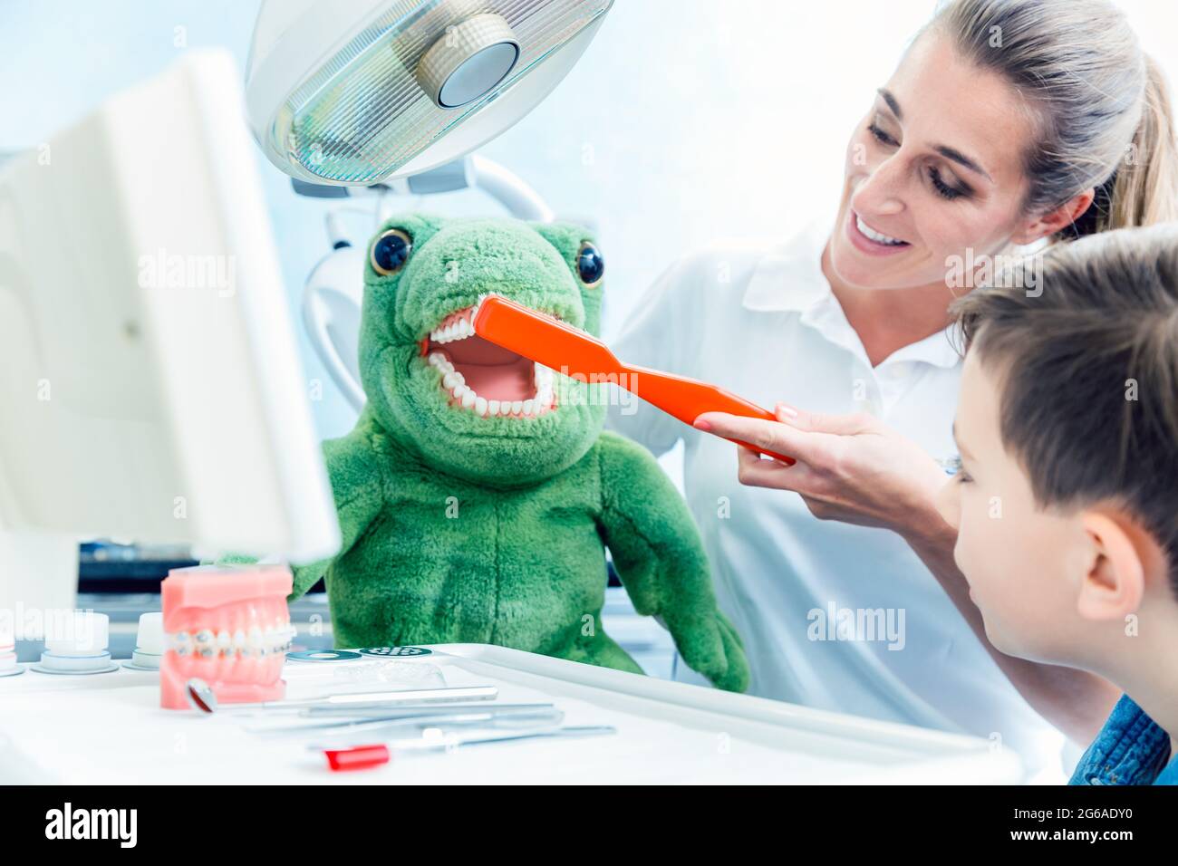 Junge, der in der Klinik den Arzt ansieht, der die Zähne des Dinosauriers putzt Stockfoto