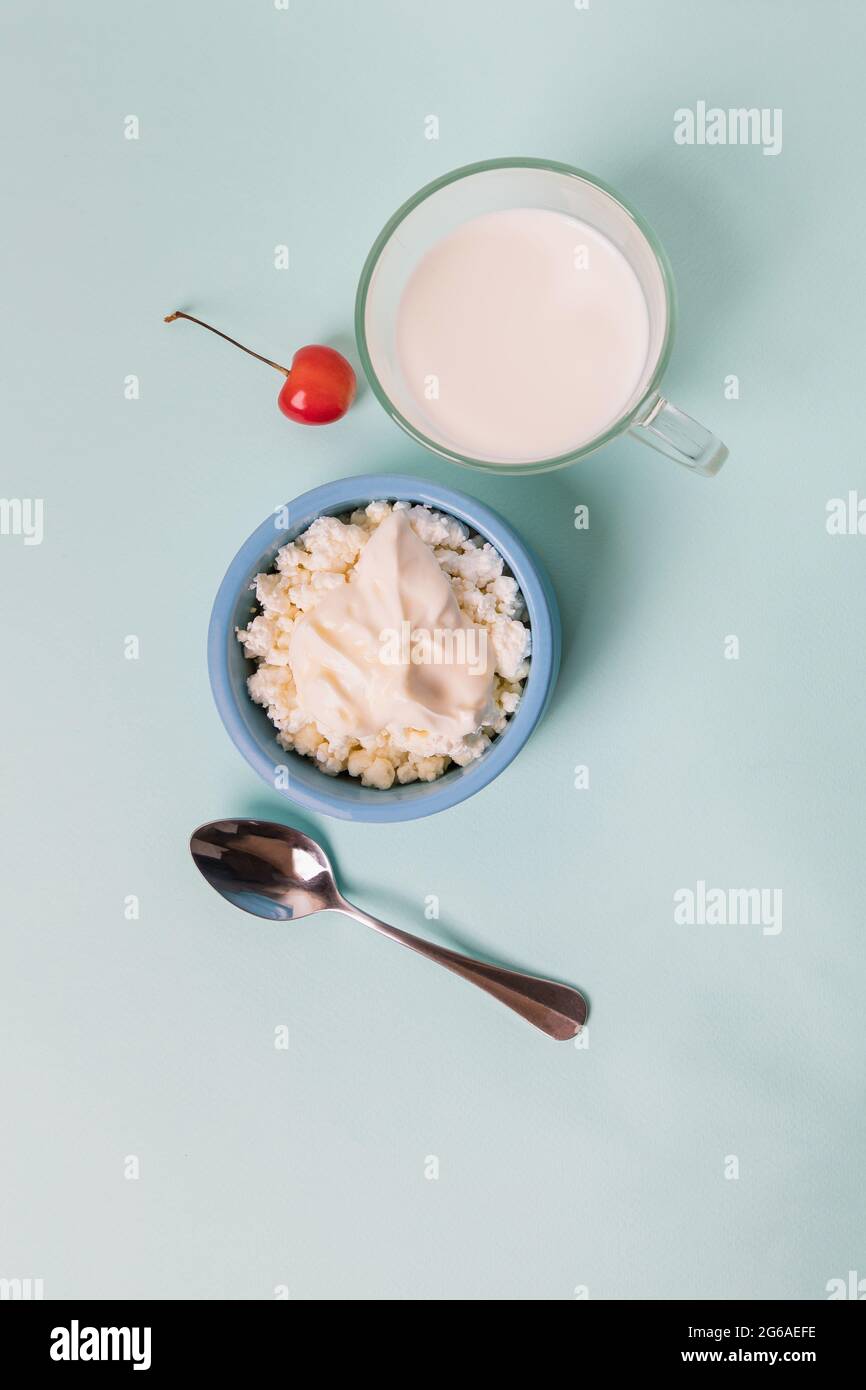 Quark in einer blauen Schüssel mit Sauerrahm und Honig, eine Tasse mit Milch. Frühstück am Morgen. Stockfoto