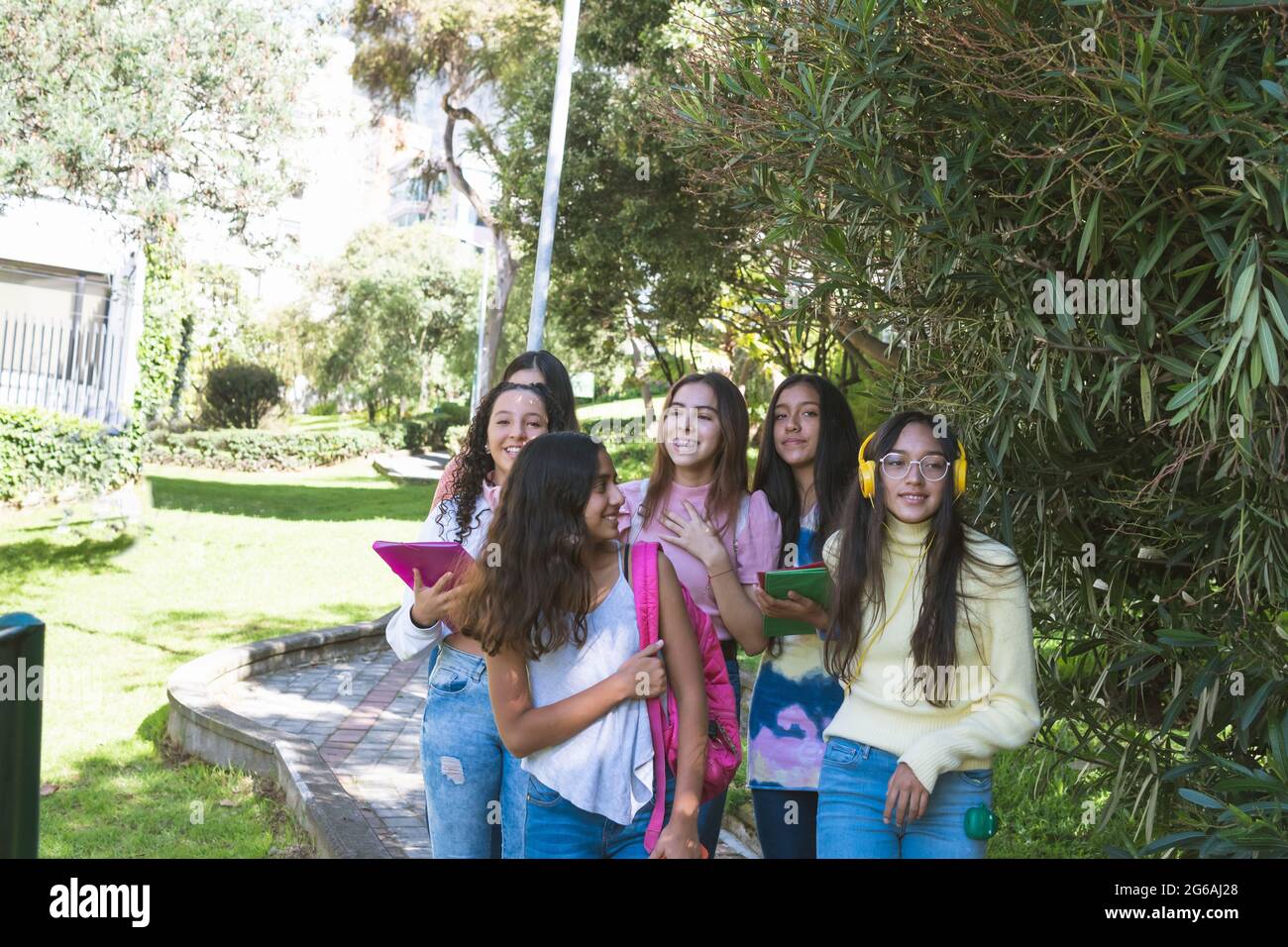 Gruppe von Latinx-Freundinnen im Teenageralter, die mit ihren Büchern und Rucksäcken lächelnd zur Schule gehen. Zurück zum Schulkonzept Stockfoto