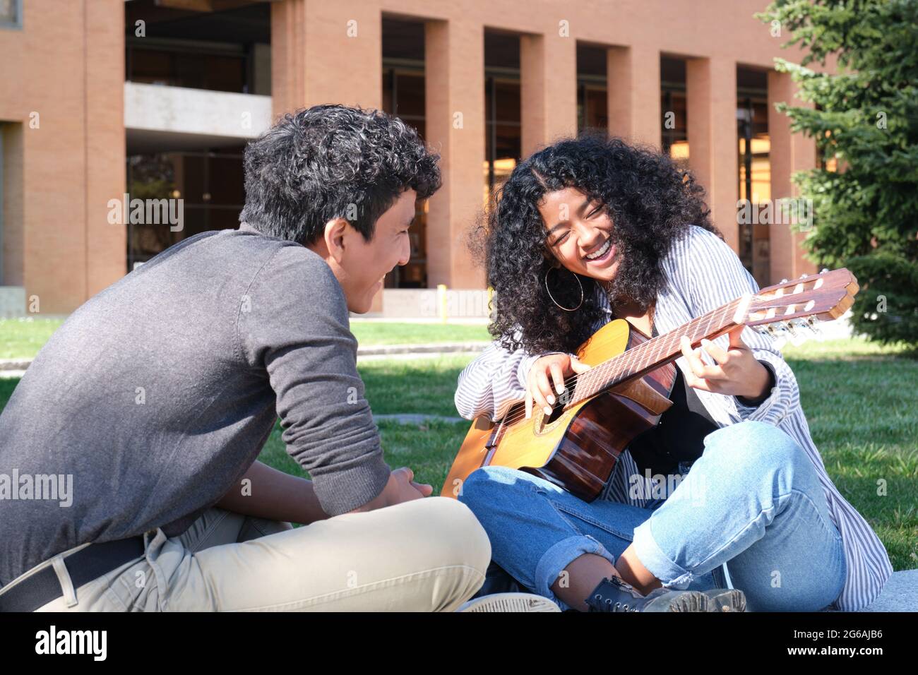 Ein junger lateinmann lehrt einer jungen lateinerin, die auf dem Universitätscampus lachend Gitarre spielt. Universitätsleben, tausendjährige Generation. Stockfoto
