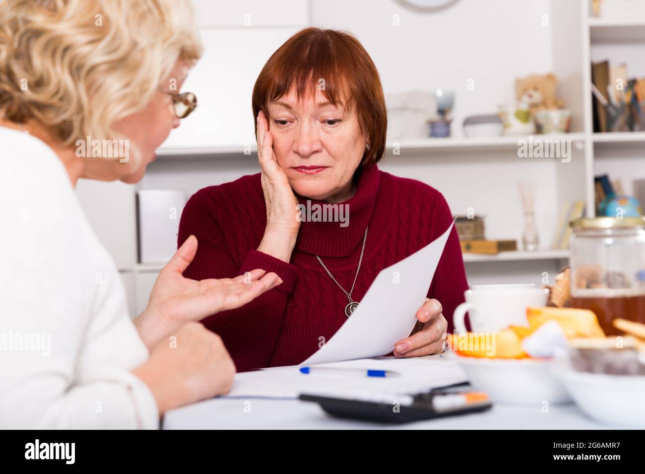 Frustrierte ältere Dame mit Dokumenten mit Frau Stockfoto