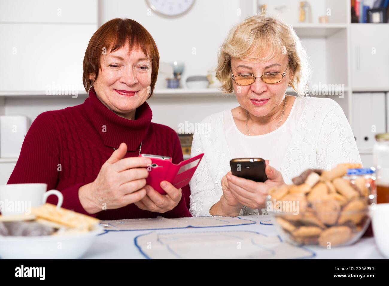 Zwei positive ältere Frauen, die Telefone benutzen Stockfoto