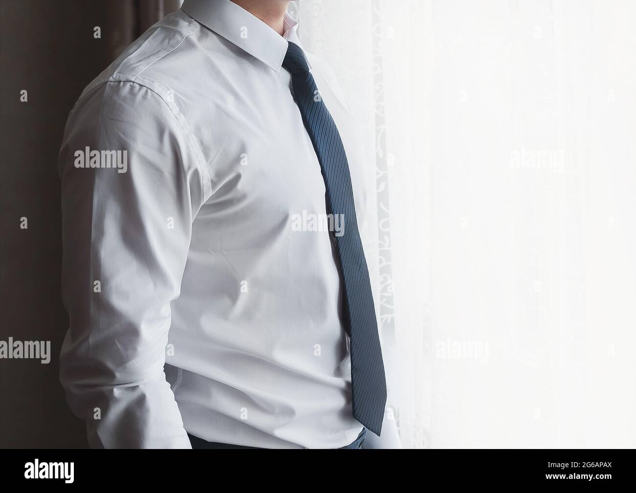 Ein Mann in einem weißen Hemd und blauer Krawatte steht vor dem Fenster. Stockfoto