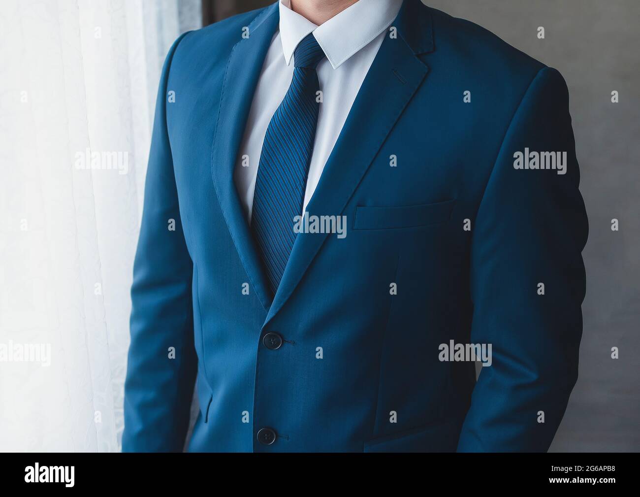 Ein Geschäftsmann in einem weißen Hemd, einem blauen Anzug mit Krawatte vor dem Fenster, einer Nahaufnahme. Stockfoto