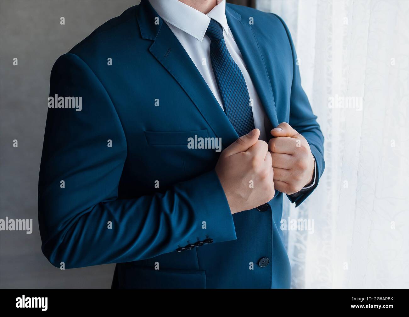 Ein Geschäftsmann in einem weißen Hemd und Krawatte passt den blauen Anzug an, der am Fenster steht. Stockfoto