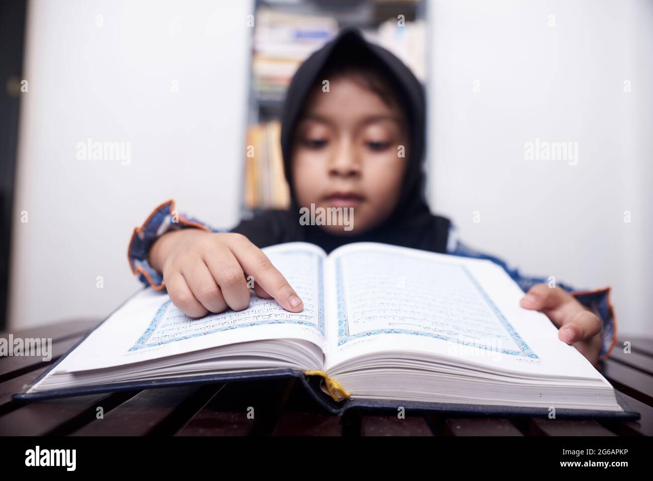 Das kleine muslimische Mädchen im Hijab liest den Koran Stockfoto