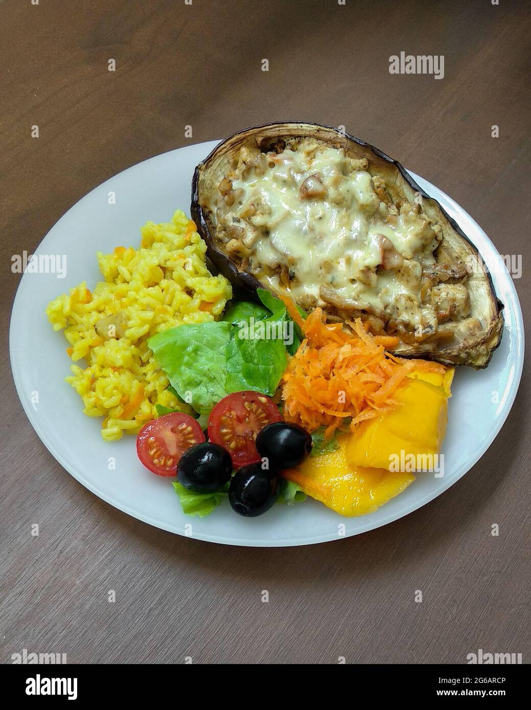 Geröstete Auberginen gefüllt mit Tofu, Pilzen und veganem Käse mit gemischtem Salat und Kurkuma-Reis auf der Seite in weißer Schale. Hausgemachtes Essen im Mittelpunkt Stockfoto