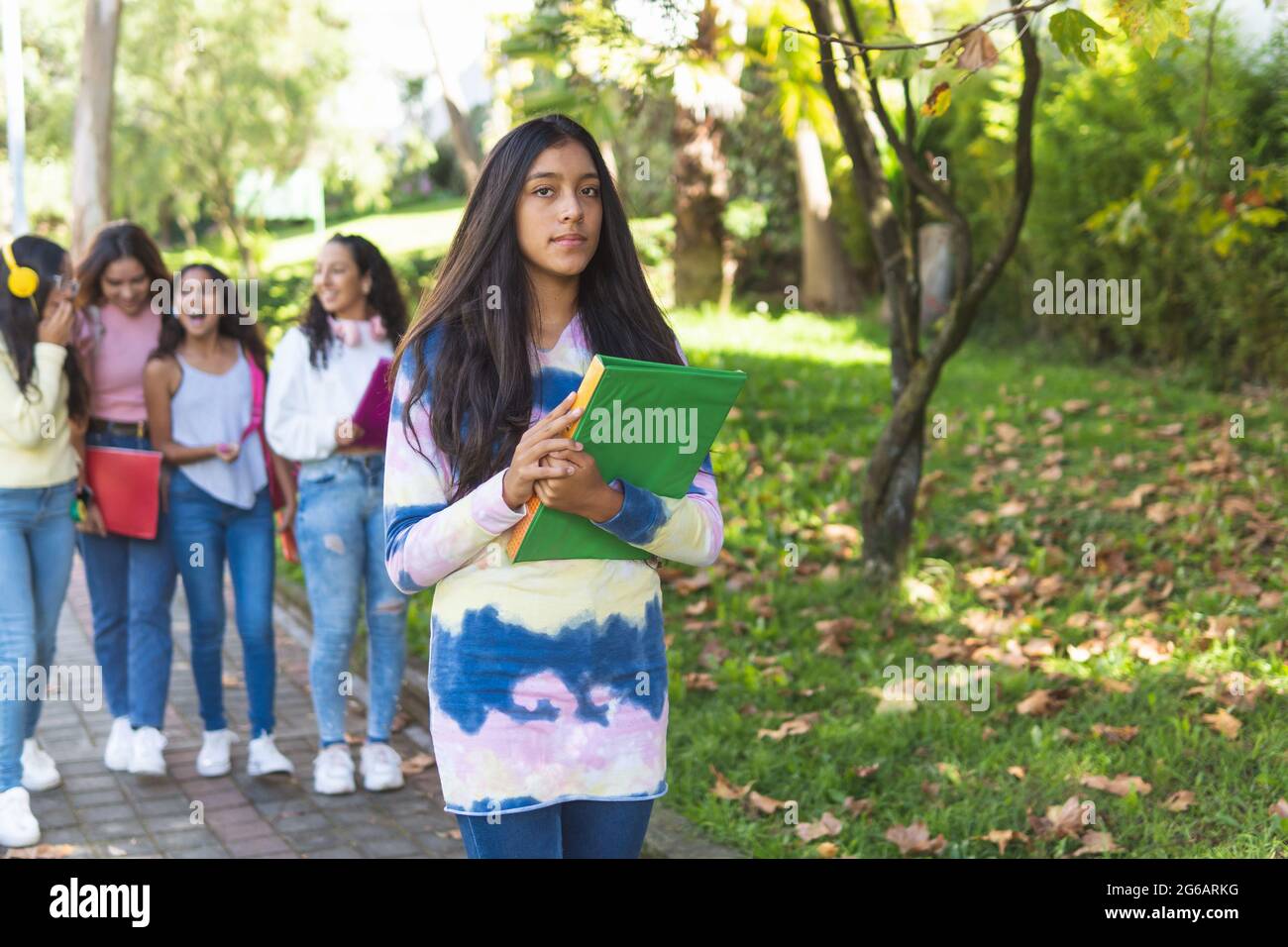 Selektiver Fokus der dunkelhäutigen Teenagerstudentin mit ihren Büchern in den Armen, die mit einer Gruppe von Klassenkameraden, die nicht fokussiert waren, auf die Kamera schaut Stockfoto