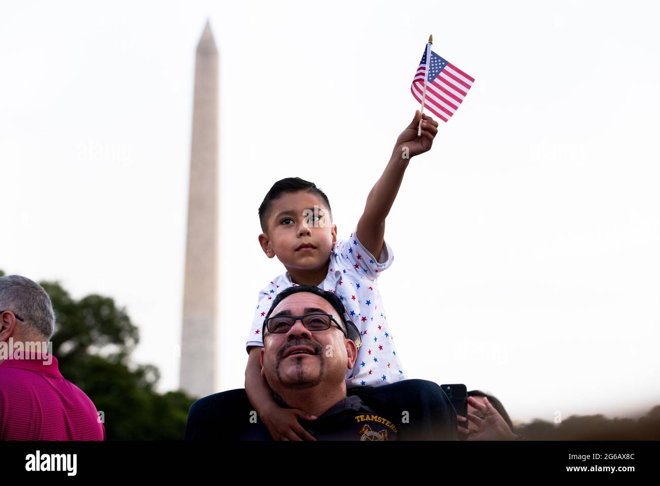 Washington, Usa. Juli 2021. Gilbert Rodriguez, sechs Jahre alt, aus Long Beach, Kalifornien, hält die US-Nationalflagge auf den Schultern seines Vaters Eddie Rodriguez, während US-Präsident Joe Biden während einer Feier des Unabhängigkeitstages in Washington, DC, USA, am 04. Juli 2021 auf dem South Lawn des Weißen Hauses eine Rede hält. Quelle: SIPA USA/Alamy Live News Stockfoto