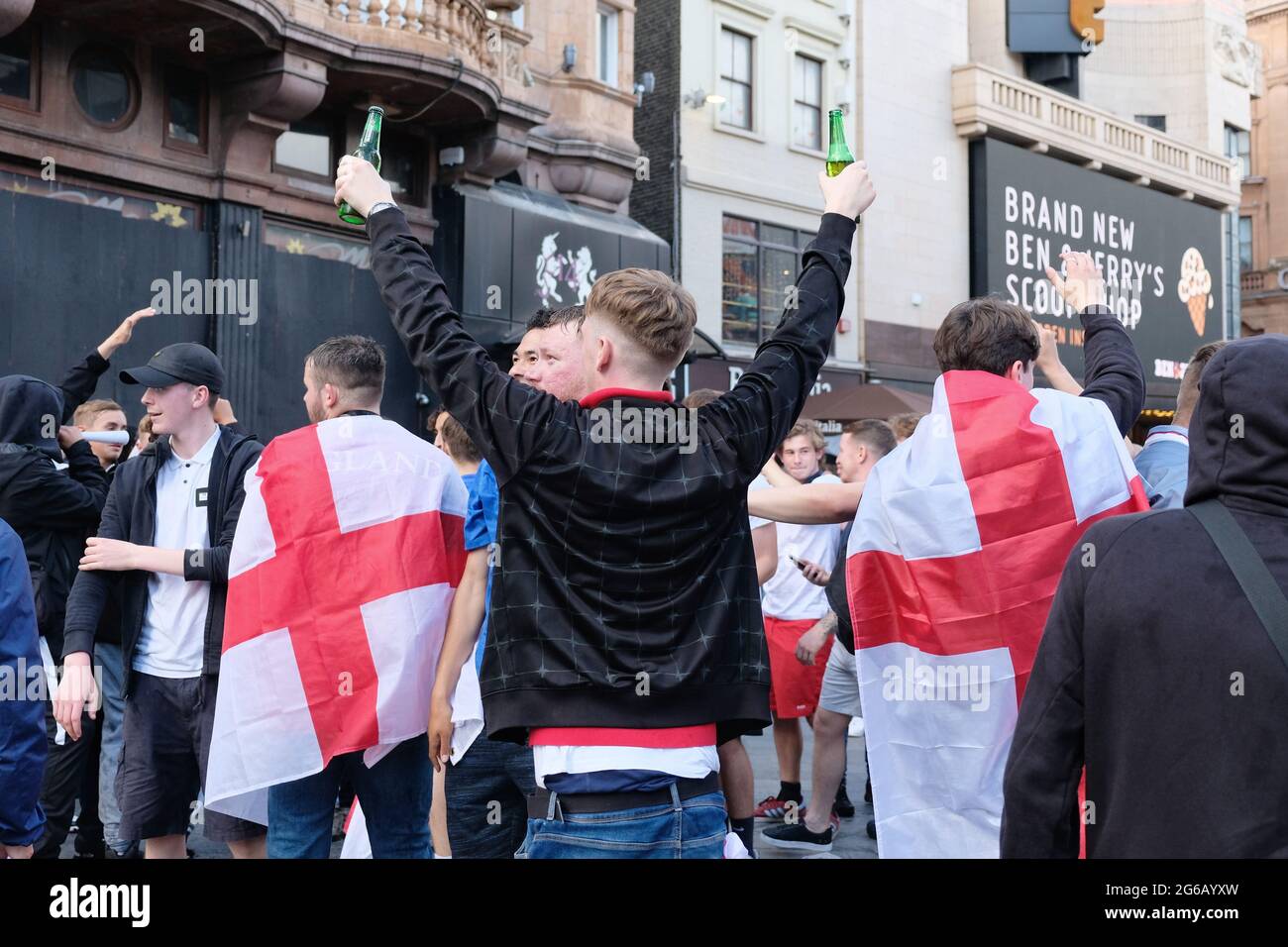 Im West End versammeln sich Fußballfans aus England. Ein Mann, der von zwei anderen Menschen flankiert wird und die Flagge von St. George trägt, hält zwei Flaschen Bier hoch. Stockfoto