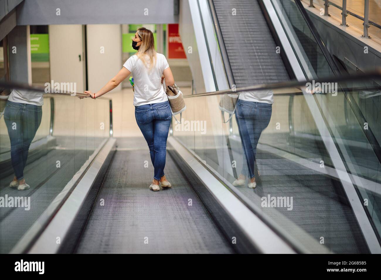 Moderne junge Frau in weißem T-Shirt und Jeans auf Rolltreppe im Einkaufszentrum schaut sich um. Einkaufen und Vergnügen. Lifestyle. Alltag in der Stadt. G Stockfoto