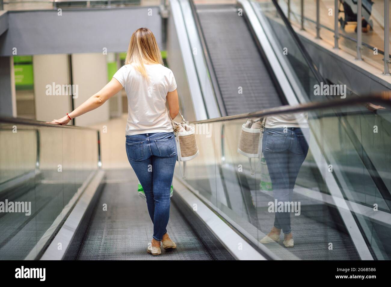 Junge Frau in weißem T-Shirt und Jeans auf Rolltreppe im Einkaufszentrum. Einkaufen und Vergnügen. Lifestyle. Alltag in der Stadt. Waren und Verbrauch Stockfoto