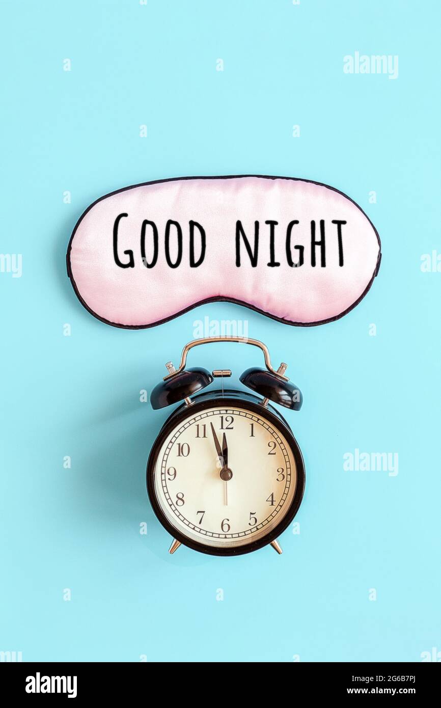 Guter Nachttext auf rosa Schlafmaske für die Augen und schwarzer Wecker auf blauem Hintergrund. Es ist Mitternacht Draufsicht. Konzept Augenschutz vor Licht für g Stockfoto