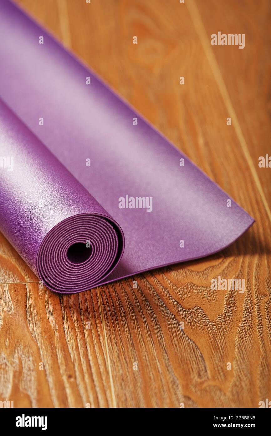 Auf dem Holzboden ist eine Flieder-Yogamatte verdreht. Gesunder Lebensstil, Sport Stockfoto