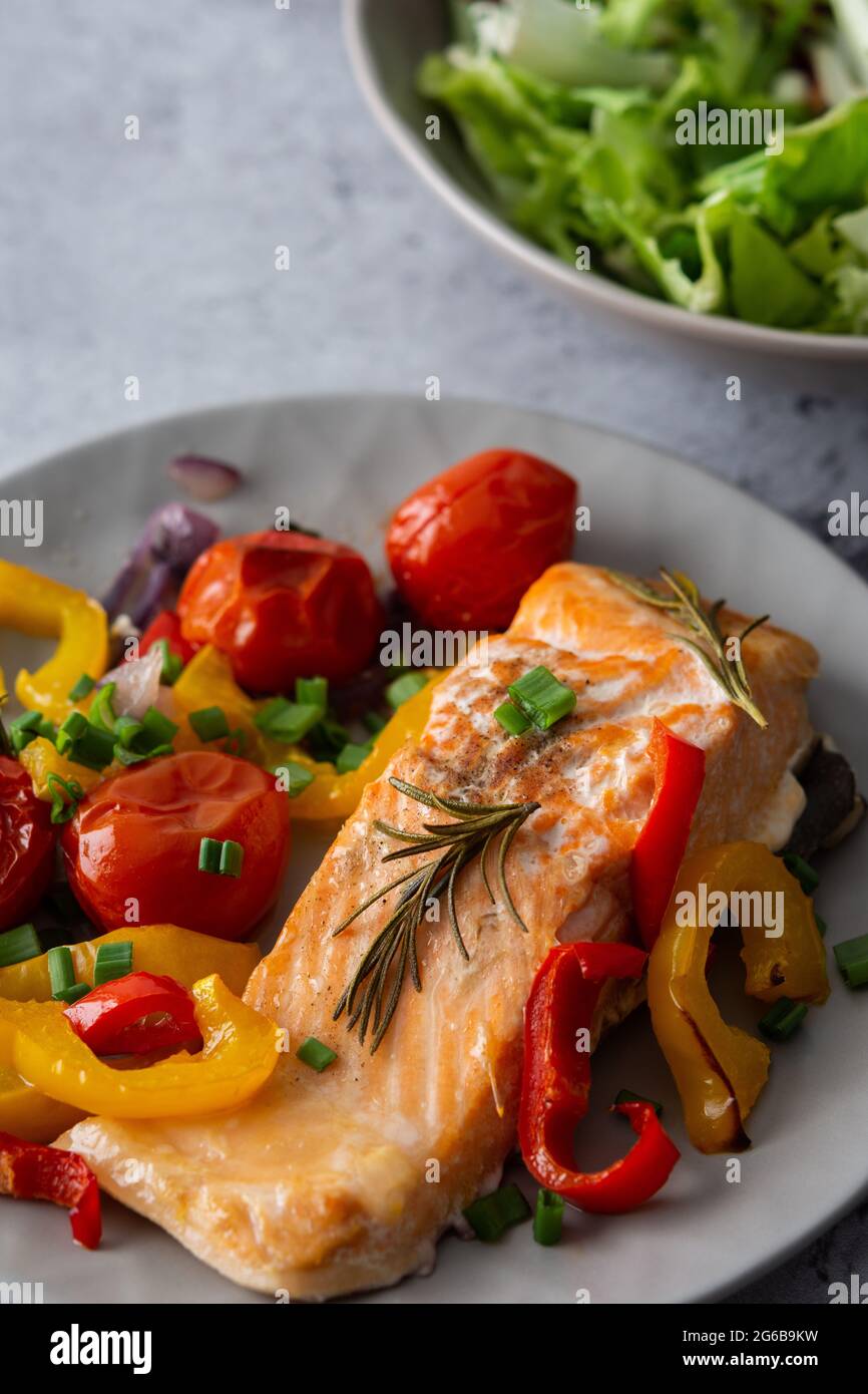 Gebackenes rotes Fischfilet Arctic Saibling auf einem Teller mit Gemüse, Salat in einer Schüssel mischen, leckeres herzhaftes gesundes Abendessen Stockfoto
