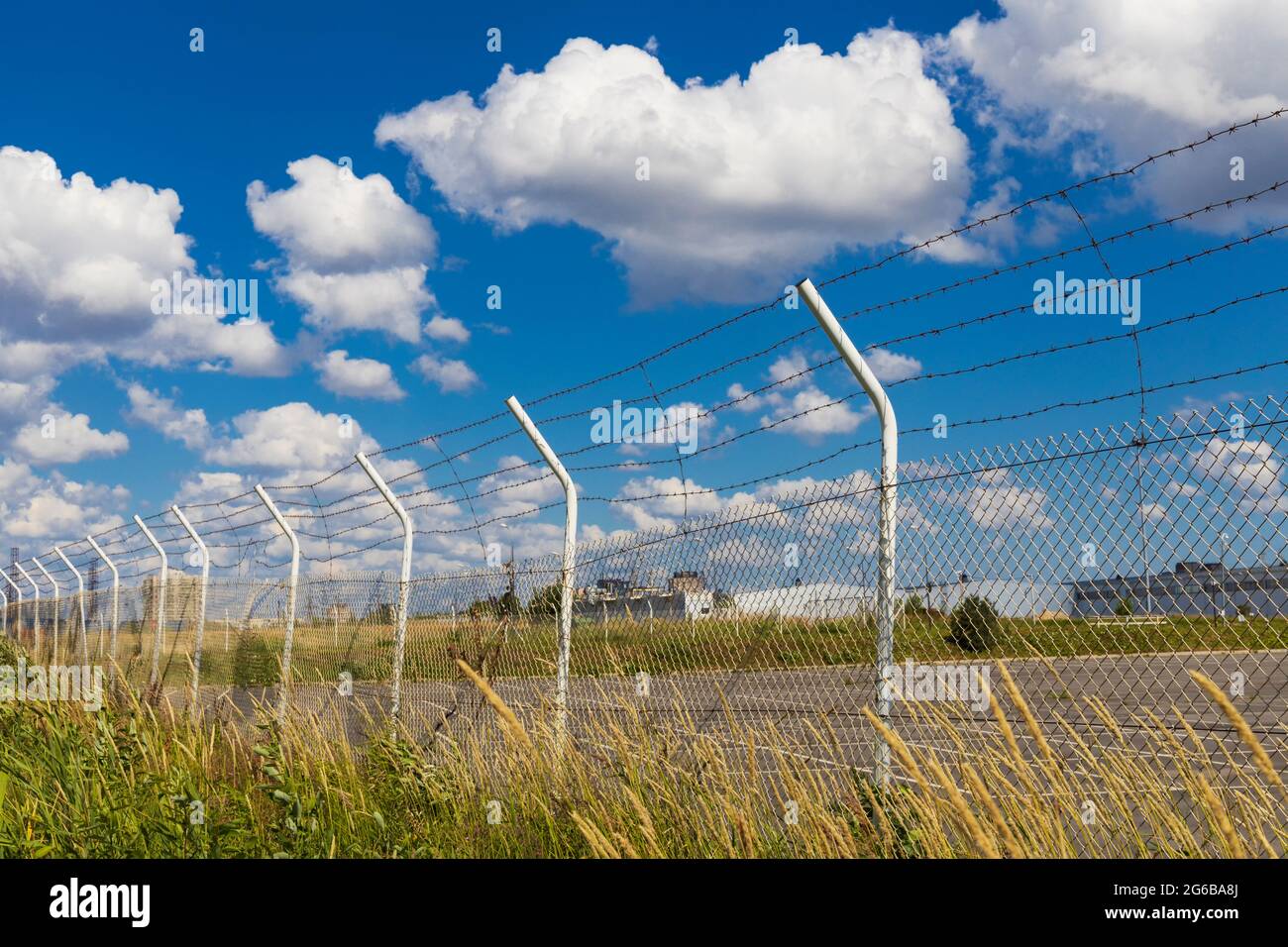 Zaun mit Reihen Stacheldraht und Pfosten im Gras auf dem Hintergrund des Himmels mit Wolken Stockfoto