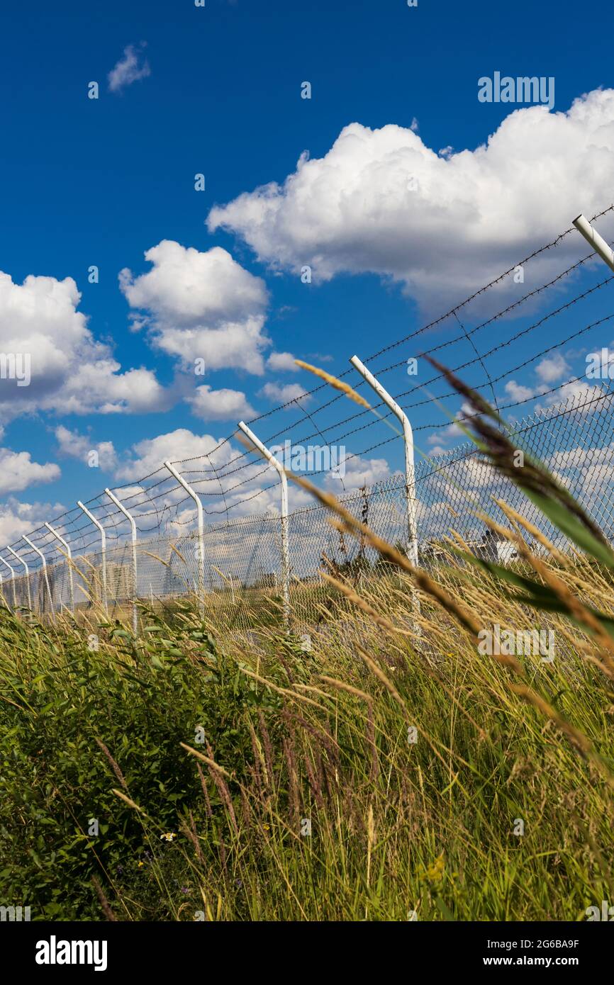 Zaun mit Reihen von Stacheldraht und Pfosten im Gras auf dem Hintergrund des Himmels mit Wolken vertikale Ausrichtung Stockfoto
