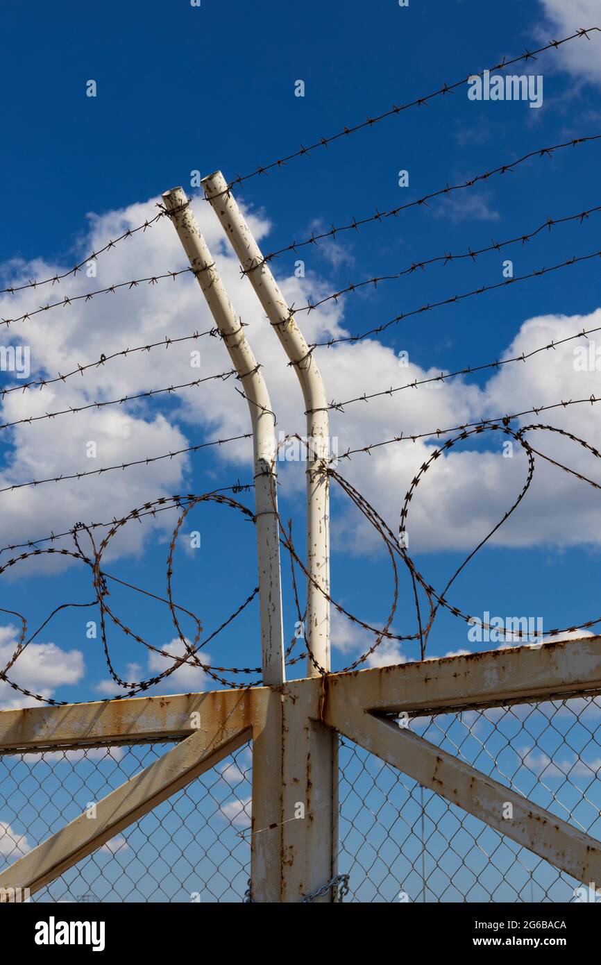 Geschlossene Tore und Pfosten mit Stacheldraht und Mesh auf dem Hintergrund des blauen Himmels Stockfoto