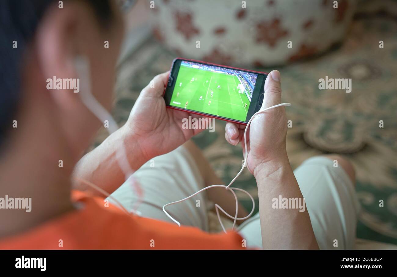 Mann, der Fußball und Sport streamt, auf dem Smartphone. Home Innenraum Hintergrund. Stockfoto