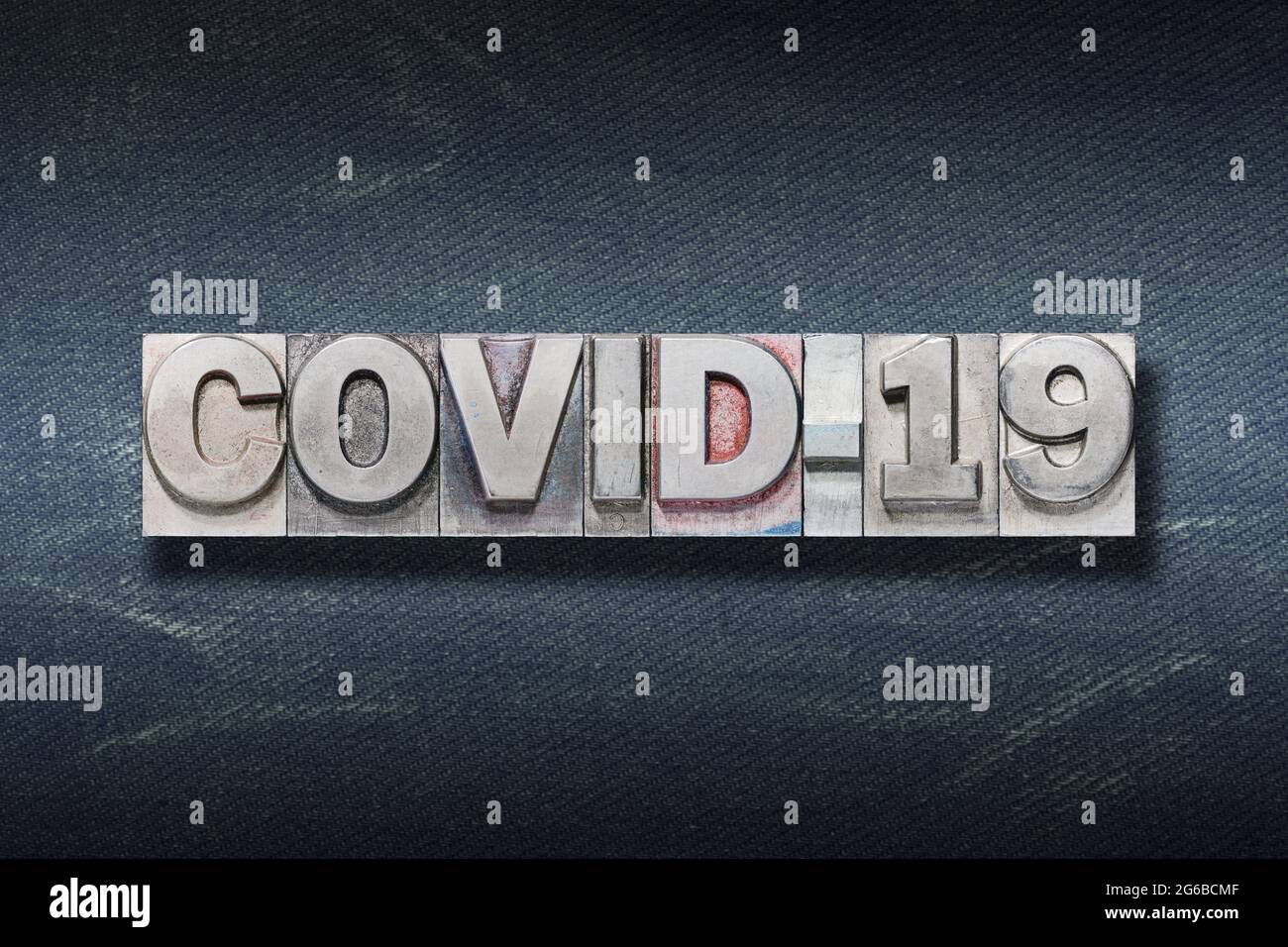 Covid-19 Coronavirus Namenskürzel aus Metallic-Buchdruck auf dunklem Jeans-Hintergrund Stockfoto