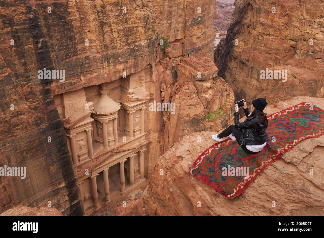 Ansicht von oben einer Frau, die auf Felsen über dem Finanzministerium sitzt, Petra, Wadi Musa, Jordanien Stockfoto