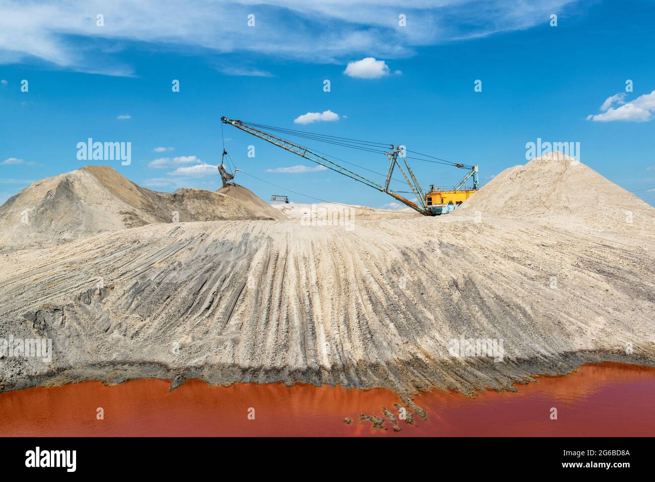 Die Industrielandschaft „ein anderer Planet“ mit einem Wanderbagger, der in einem Titansteinbruch mit einer intensiven roten Farbe von Wasser arbeitet Stockfoto