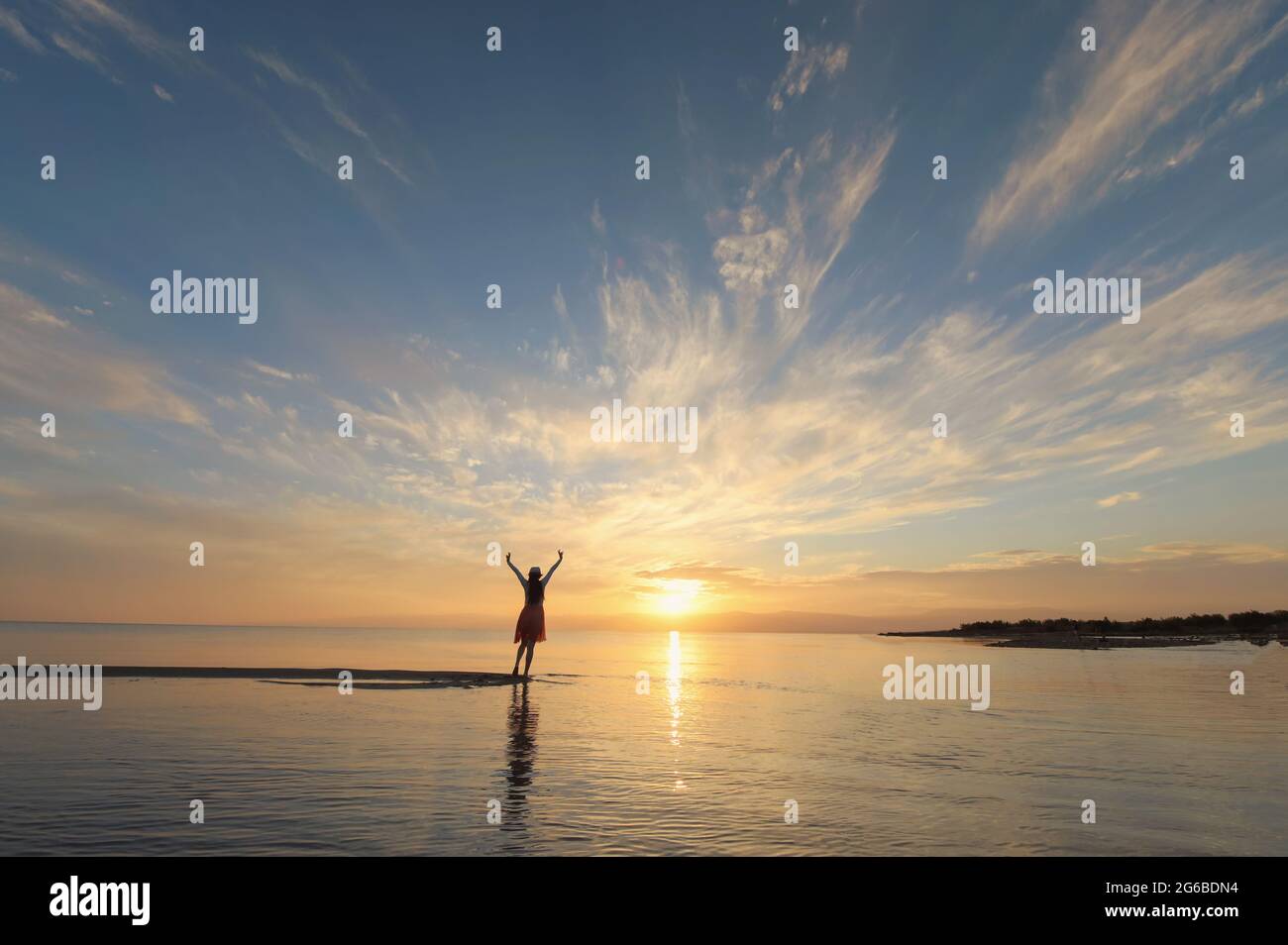 Rückansicht einer Frau, die bei Sonnenuntergang am Strand mit ihren Armen in der Luft steht, Thailand Stockfoto