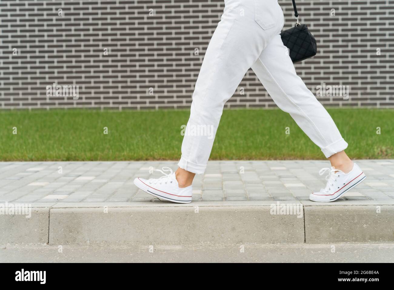 Frauenbeine in weißen Hosen, die an einer Backsteinmauer vorbeilaufen Stockfoto