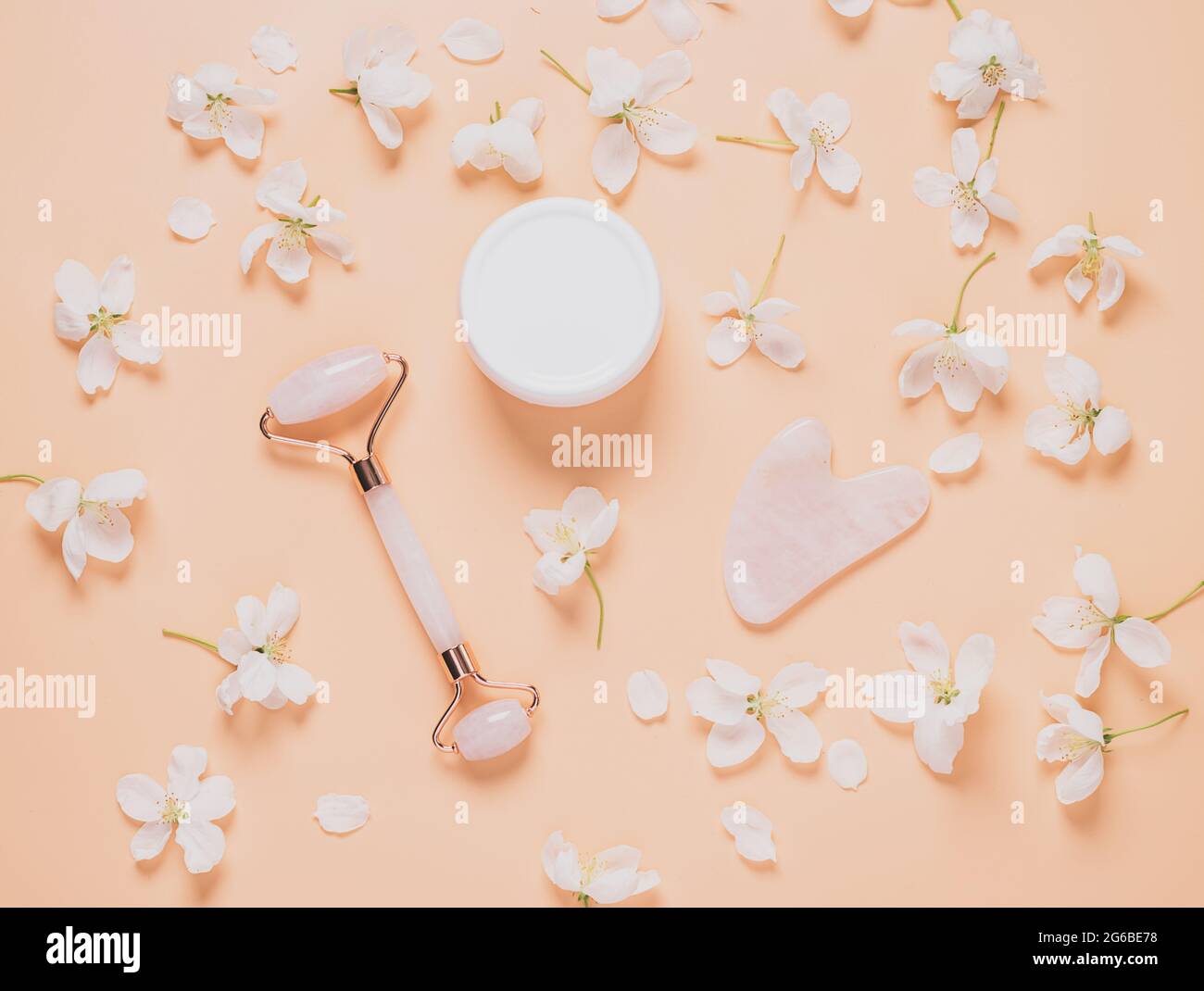 Gesichtsmassage-Set Roller Scraper guasha kosmetisches Öl Serum Gesichtspflege auf pastellrosa Hintergrund Stockfoto