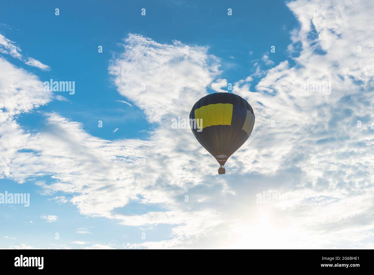 Heißluftballon und blauer Himmel, Sonne, weiße Wolke.Blauer gelber Heißluftballon in der Luft am Sommerabend. Stockfoto
