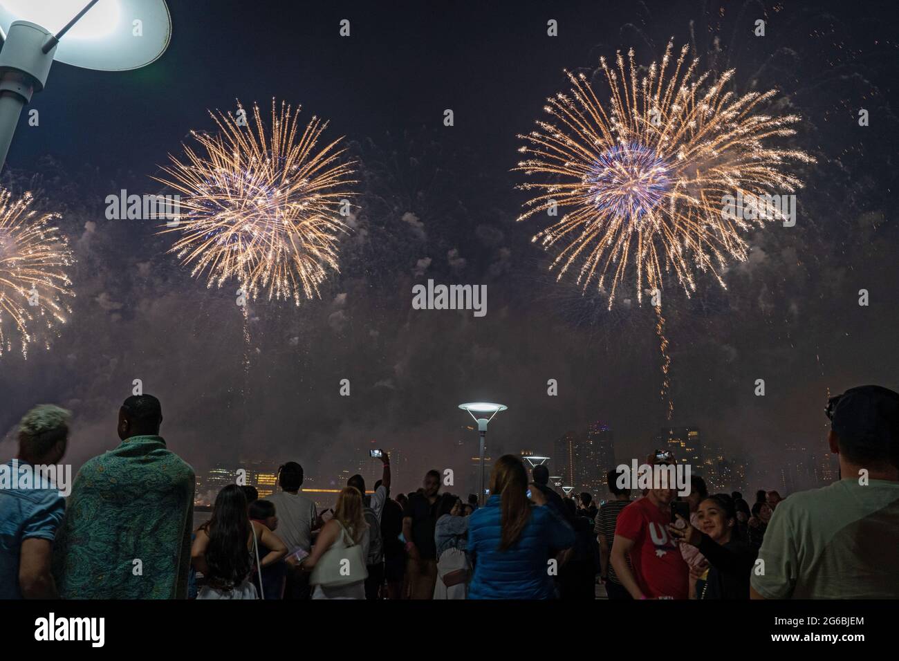 NEW YORK, NY - JULI 04: Zuschauer beobachten das Feuerwerk während der 45. Jährlichen Macy's Feuerwerksschau am 4. Juli 2021 mit Blick auf die Skyline von Manhattan am Gantry State Plaza in Long Island City im Stadtteil Queens von New York City. Als Beweis für die Verbesserung der Stadt gegenüber COVID-19 war die diesjährige Feier mit einer Laufzeit von 25 Minuten größer und länger als in den Vorjahren geplant. Aufgrund der Coronavirus-Pandemie des vergangenen Jahres wurde das Feuerwerk über vier Nächte und mehrere Bezirke verteilt, um Versammlungen zu begrenzen und die Ausbreitung zu verlangsamen. Kredit: Ron Adar/Alamy Stockfoto