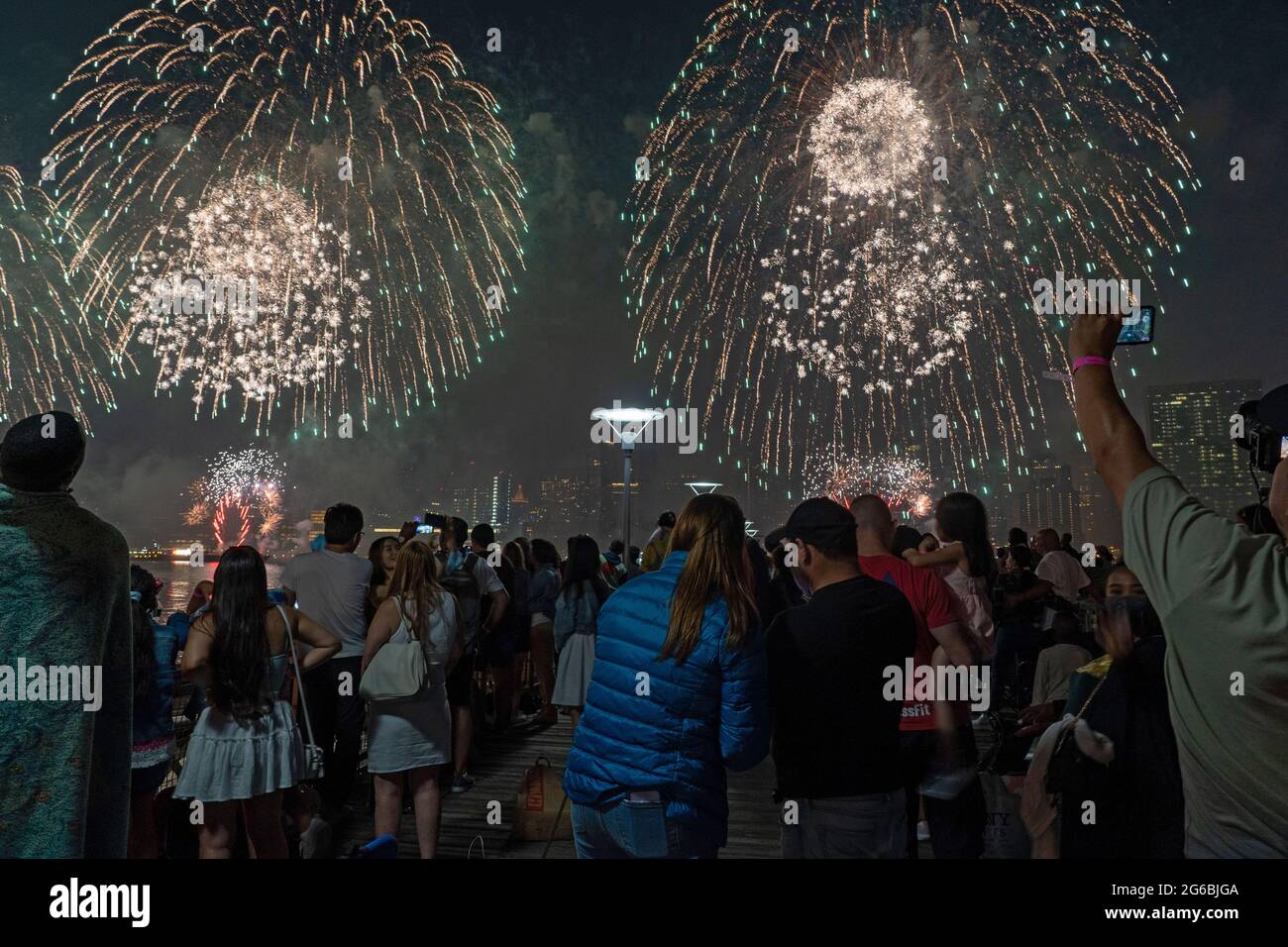 NEW YORK, NY - JULI 04: Zuschauer beobachten das Feuerwerk während der 45. Jährlichen Macy's Feuerwerksschau am 4. Juli 2021 mit Blick auf die Skyline von Manhattan am Gantry State Plaza in Long Island City im Stadtteil Queens von New York City. Als Beweis für die Verbesserung der Stadt gegenüber COVID-19 war die diesjährige Feier mit einer Laufzeit von 25 Minuten größer und länger als in den Vorjahren geplant. Aufgrund der Coronavirus-Pandemie des vergangenen Jahres wurde das Feuerwerk über vier Nächte und mehrere Bezirke verteilt, um Versammlungen zu begrenzen und die Ausbreitung zu verlangsamen. Kredit: Ron Adar/Alamy Stockfoto